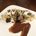 In a cozy corner of a little pastry shop, where the air smells of cocoa and roasted nuts, lives the Chocolate Almond Cluster Cannolo. Its crisp golden shell takes a dip into a pool of rich, melted chocolate before being gently rolled through a snowfall of toasted almonds that glimmer like tiny jewels. Inside, a velvety almond cream waits, smooth and sweet as a whispered secret. At each end, clusters of chocolate and almonds huddle together like friends on an autumn night, ready to greet each lucky bite. 