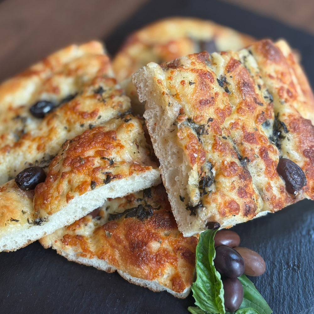 Enjoy the flavours of Italy with our Authentic House-Made Focaccia, topped with Kalamata olives and aromatic basil. This soft, pillowy bread is baked to golden perfection, offering a delicate balance of savoury olive richness and the fresh, fragrant essence of basil. With its irresistible texture and bold flavors, our focaccia makes the perfect accompaniment to any meal or a delicious standalone treat. Made fresh daily, it’s a true taste of Italy in every bite