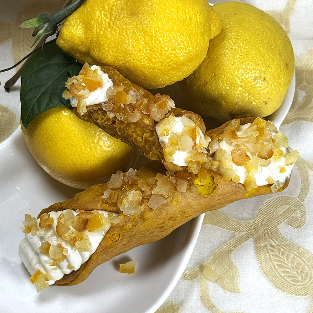 Bright, silky, and irresistibly fresh, our Yuzu Cannoli captures the spirit of citrus in its most refined form. The housemade yellow pastry shell offers a delicate crunch and sunny hue, perfectly complementing the vibrant yuzu-infused cream within. Each cannoli is finished with glistening candied citrus peel, adding a touch of sparkle and a sweet-tart accent to every bite. A harmony of zesty brightness and Italian tradition, this creation is pure sunshine wrapped in pastry.